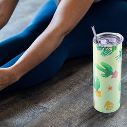 Tumbler with cactus design on a wooden surface next to a person wearing blue leggings.