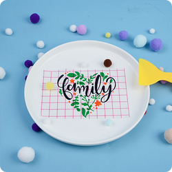 White plate with 'family' design on a blue background with colorful pom-poms.