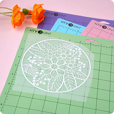 Floral design stencil on a green cutting mat with orange flowers and HTV cutters in the background.