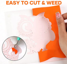 Hand holding a pink paper cutout with a decorative design, placed on an orange sheet of paper.