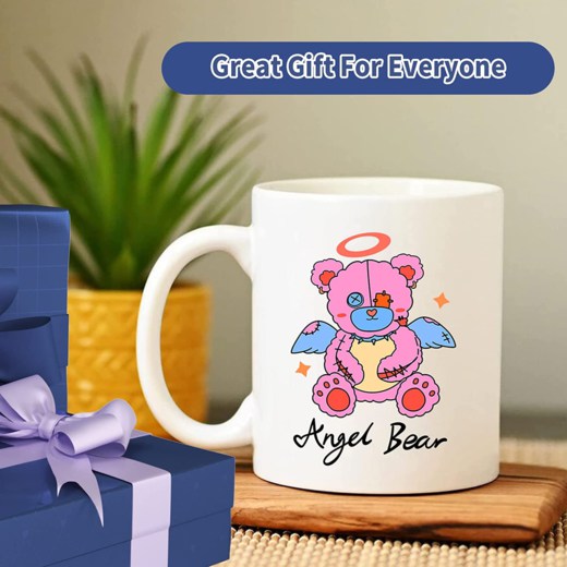 White mug with an angel bear design and text 'Angel Bear' on a wooden surface, with presents and a plant in the background.